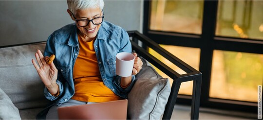 Selbsthilfegruppen zum Thema Blasenbeschwerden im Internet Frau mit entspanntem und glücklichen Gesichtsausdruck am Laptop und mit einer Tasse Tee in der Hand, die online in einer Selbsthilfegruppe zum Thema Blasenbeschwerden unterwegs ist