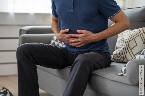Mann sitzend auf einer Couch mit sichtbaren Schmerzen wegen einer chronischen Blasenentzündung