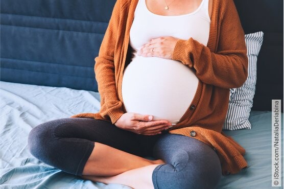 Hochschwangere Frau auf ihrem Bett sitzend